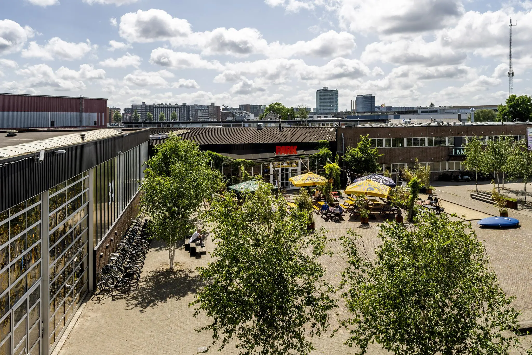 Binnenplein aan de Johan van Hasseltweg met terrastafels, parasols en omliggende bedrijfsgebouwen op een zonnige dag.