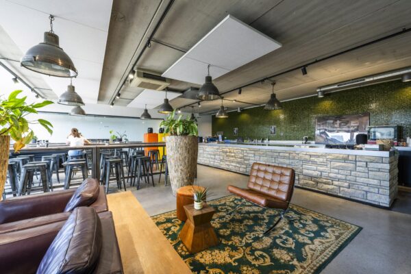 Moderne, industrieel ingerichte lounge- en eetruimte aan de Johan van Hasseltweg met bar, hoge tafels, planten en leren stoelen.