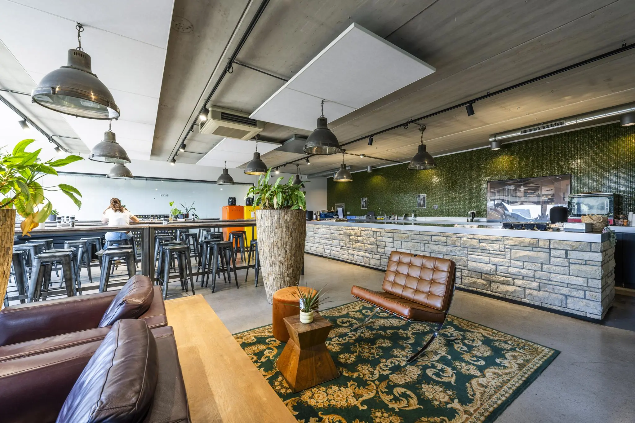 Moderne, industrieel ingerichte lounge- en eetruimte aan de Johan van Hasseltweg met bar, hoge tafels, planten en leren stoelen.
