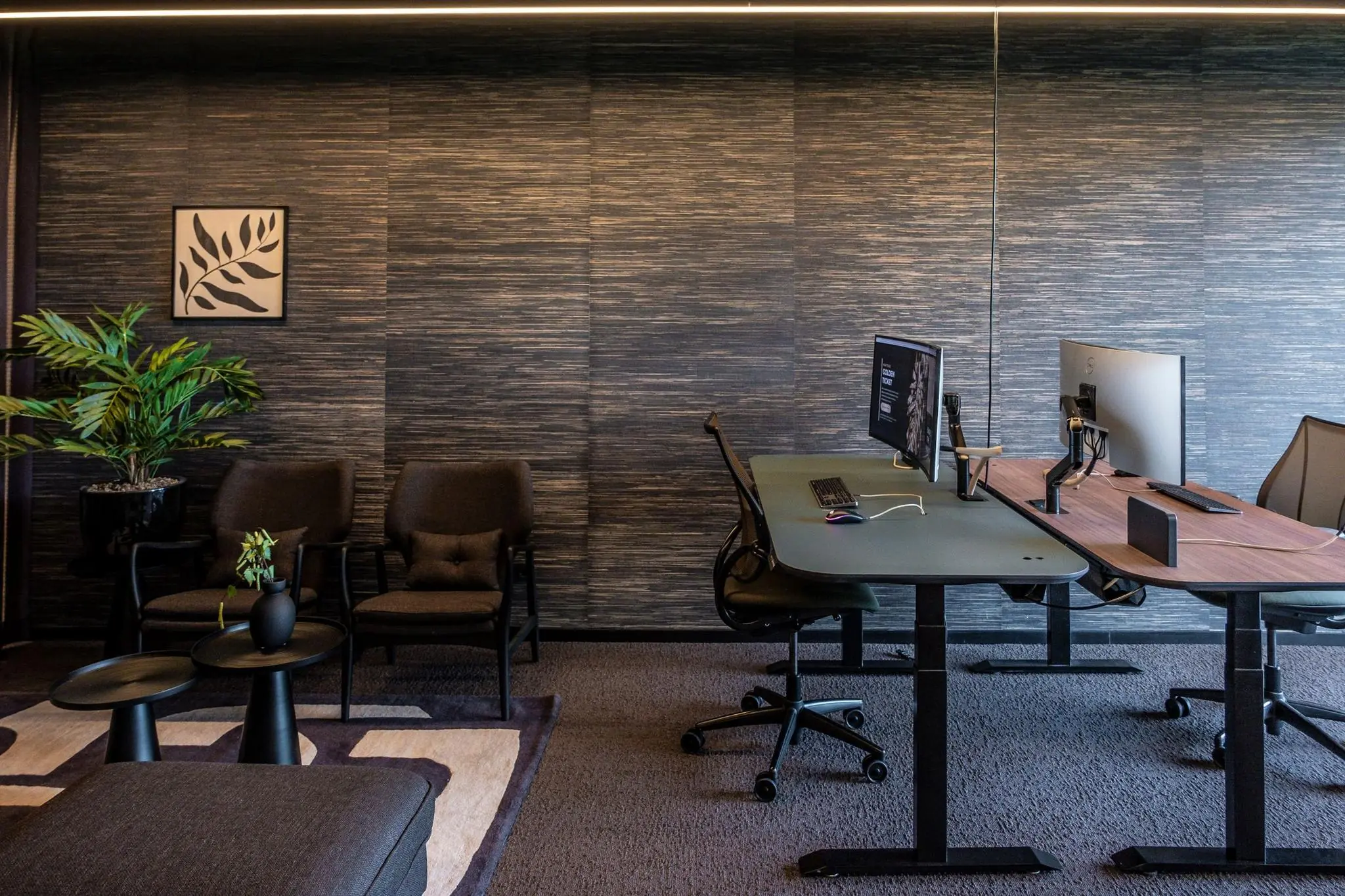 Moderne kantoorruimte met zitgedeelte, planten en verstelbare bureaus met computerschermen.