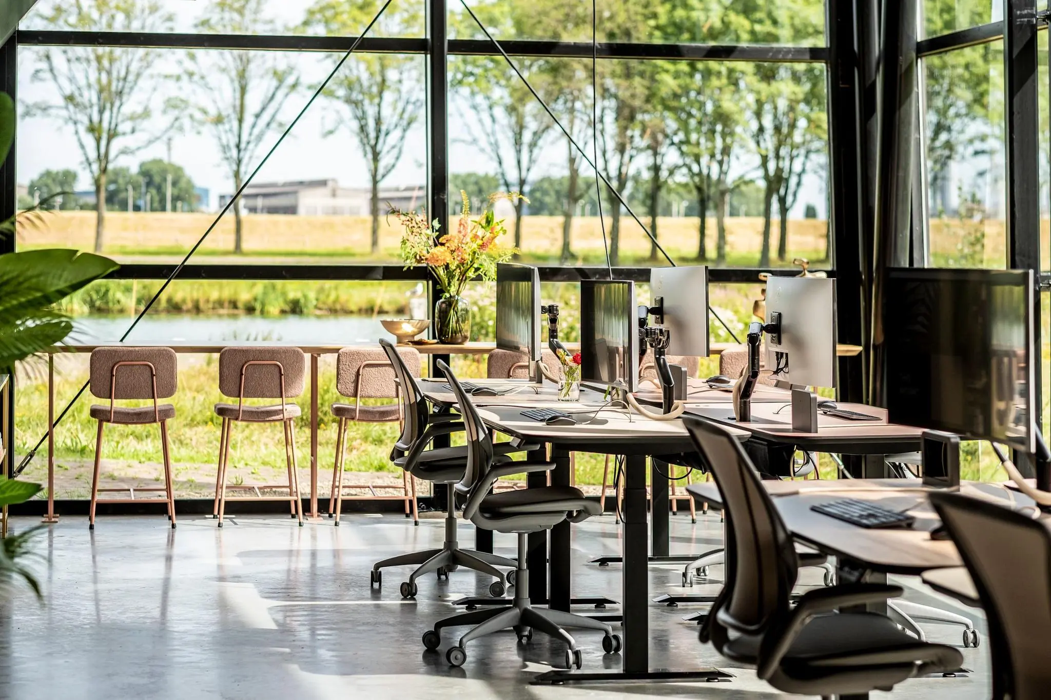 Moderne, open kantoorruimte aan de Plaatweg met werkplekken, computers en uitzicht op het groen en water buiten.