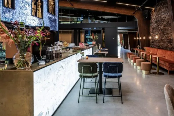 Modern ingericht café met marmeren bar, fluwelen zitplaatsen en warme verlichting aan de Plaatweg.