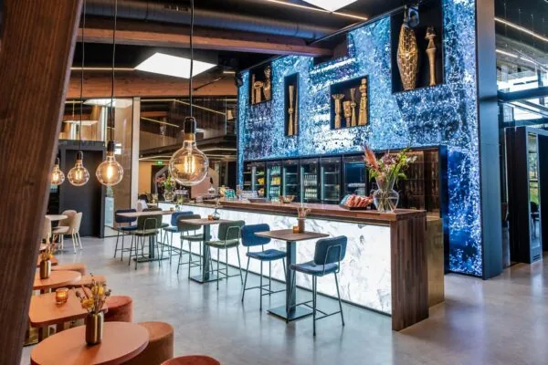 Moderne en sfeervol ingerichte bar met kunstzinnige wanddecoratie, hoge zitplaatsen en warme verlichting aan de Plaatweg.