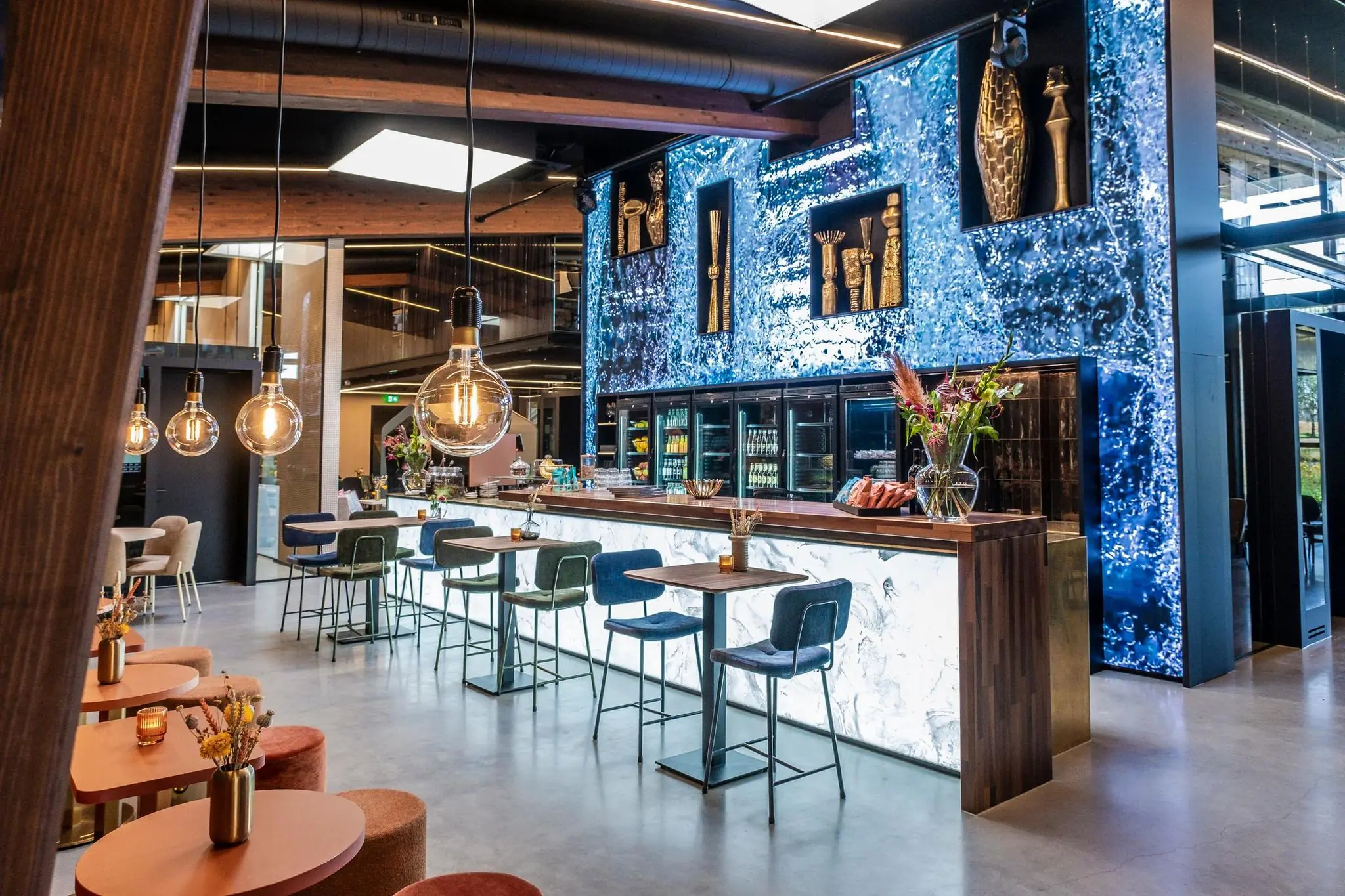 Moderne en sfeervol ingerichte bar met kunstzinnige wanddecoratie, hoge zitplaatsen en warme verlichting aan de Plaatweg.