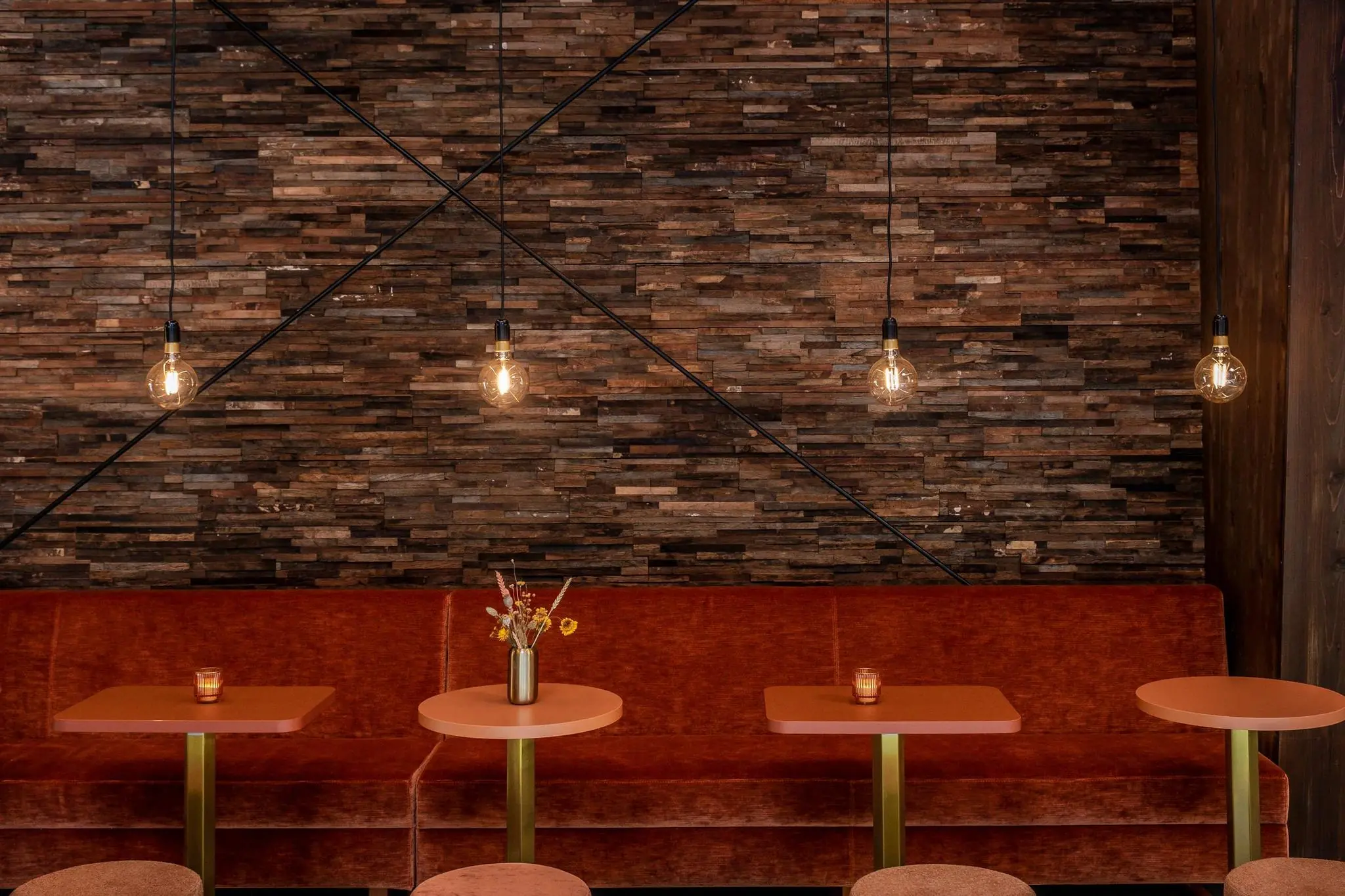 Sfeervol ingericht café met een roodfluwelen bank, ronde tafels, hanglampen en een wand van donker hout.