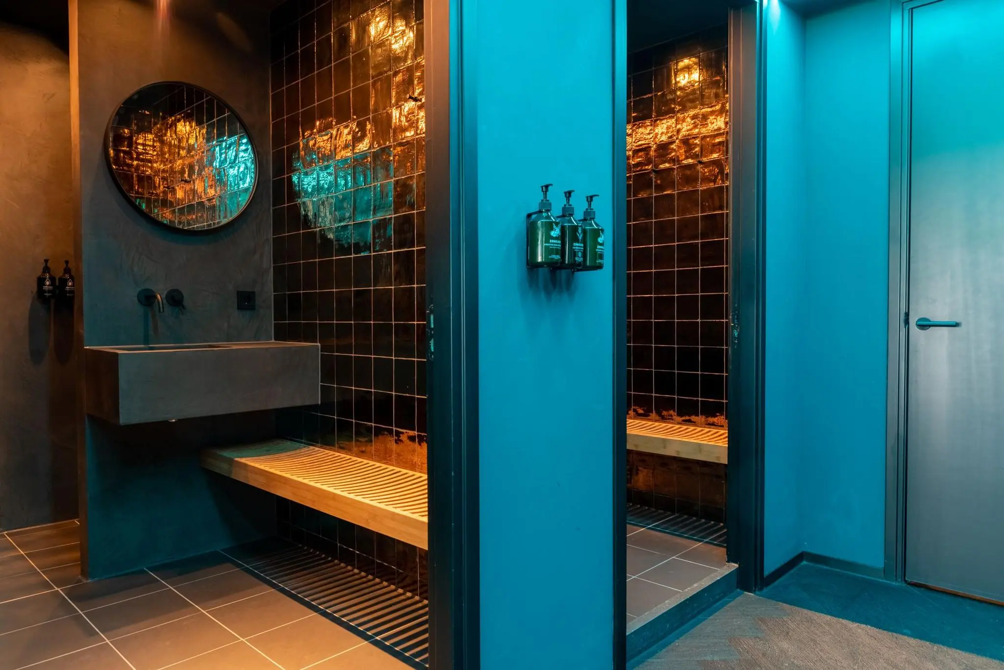 Moderne wellnessruimte met zwarte glanzende tegels, houten zitbank, betonnen wastafel en sfeerverlichting.