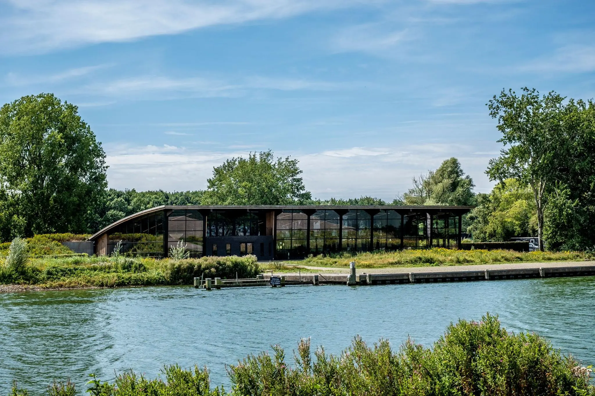 Modern gebouw aan de Plaatweg met glazen gevel, omringd door groen en gelegen aan het water.