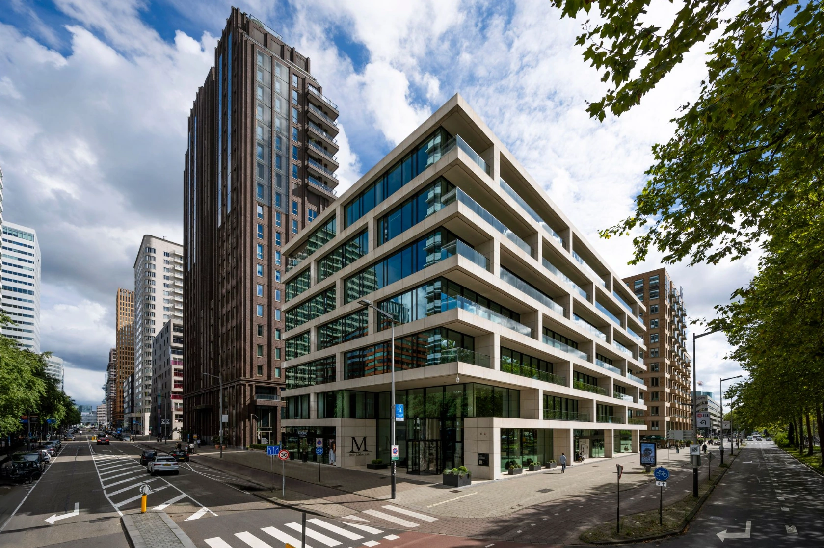 Modern hoekgebouw aan de Gustav Mahlerlaan in Amsterdam met glazen gevels en omliggende hoogbouw.