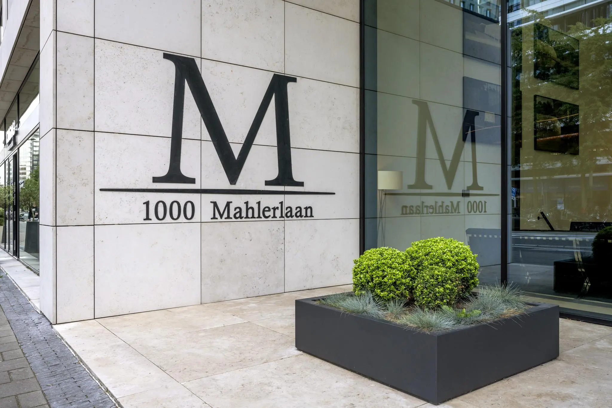 Vooraanzicht van het kantoorpand aan de Gustav Mahlerlaan 1000 met groot zwart logo op de gevel.