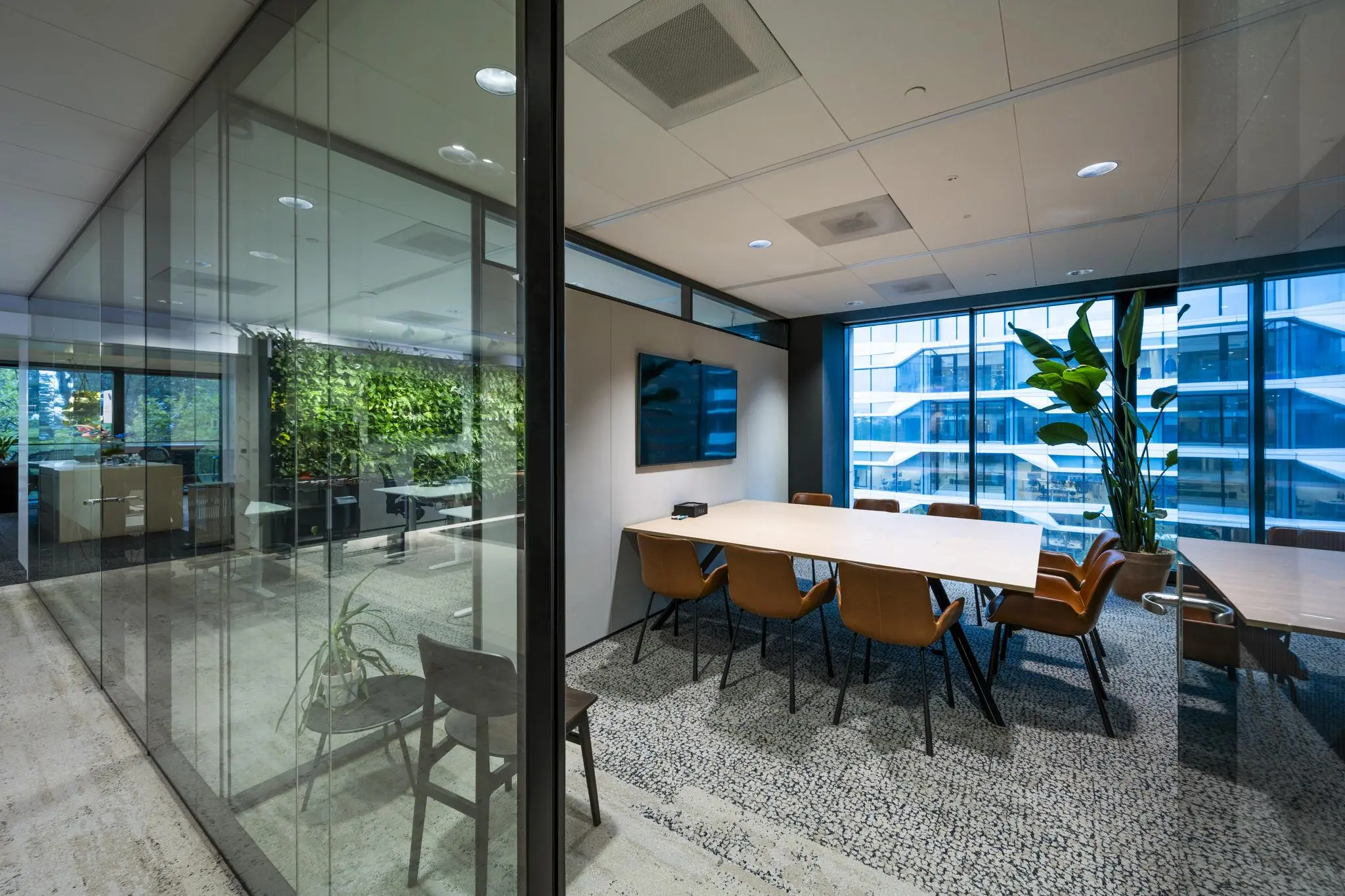 Moderne vergaderruimte aan de Gustav Mahlerlaan met glazen wanden, leren stoelen, groot scherm en uitzicht op een kantoorgebouw.