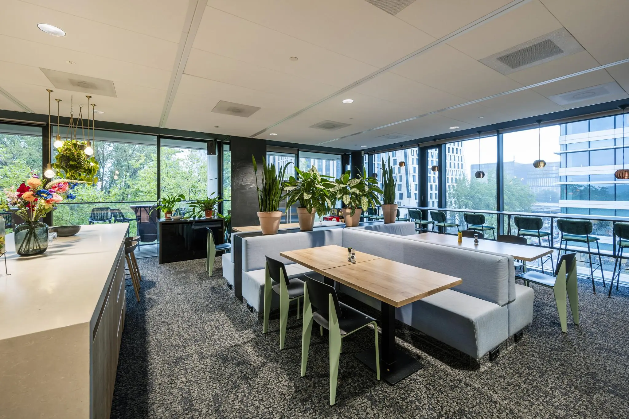 Moderne kantoorlounge aan de Gustav Mahlerlaan met zitplekken, veel planten en grote ramen met uitzicht op kantoorgebouwen.