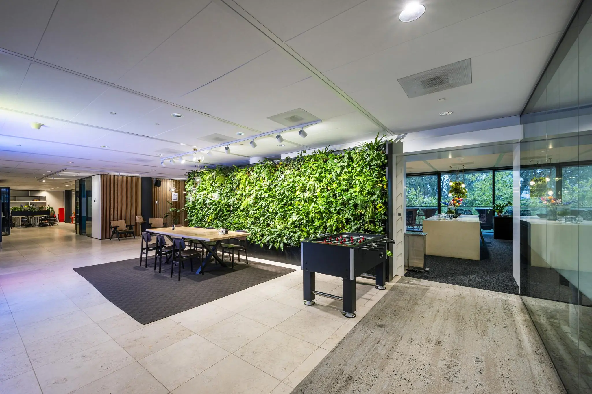 Moderne kantoorlounge aan de Gustav Mahlerlaan met groene plantenwand, tafelvoetbaltafel en zithoeken.