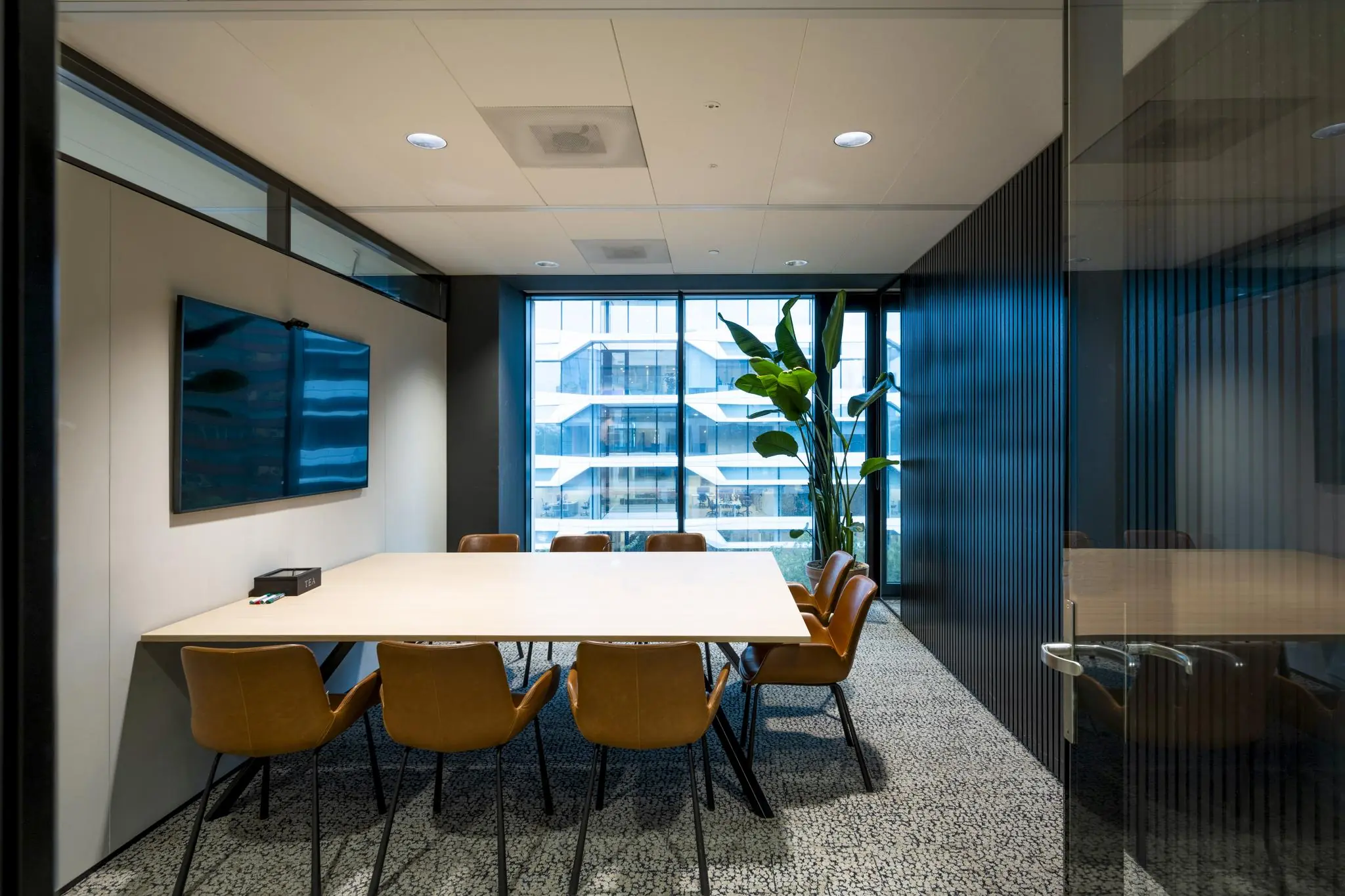Vergaderruimte aan de Gustav Mahlerlaan met moderne inrichting, grote tafel, leren stoelen, een flatscreen en uitzicht op een modern kantoorgebouw.