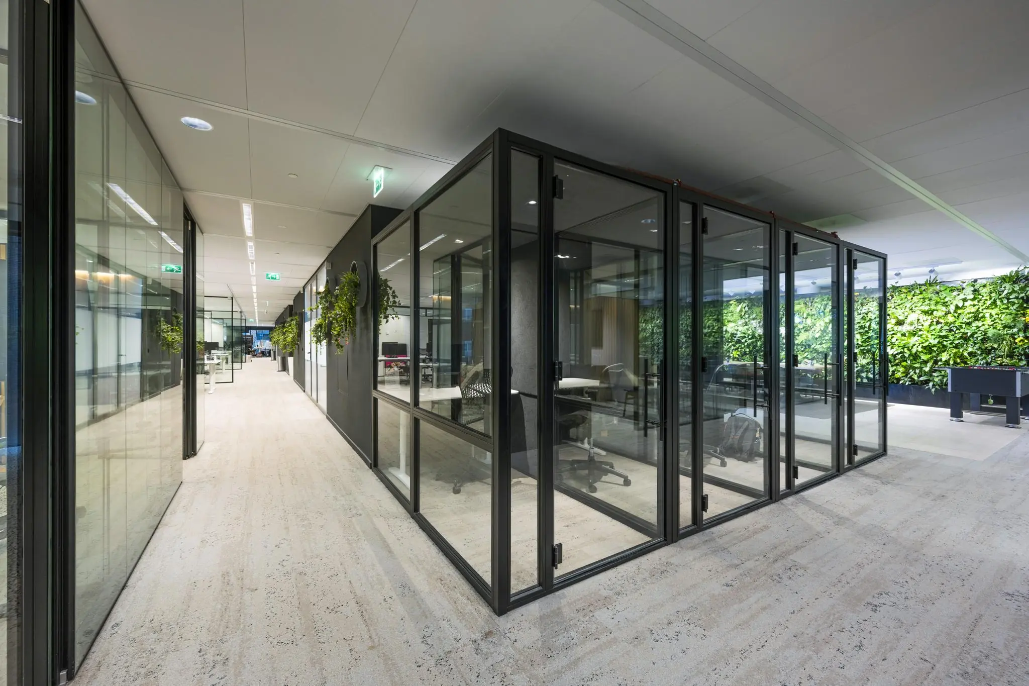 Moderne kantoorruimte aan de Gustav Mahlerlaan met glazen vergaderruimtes, groene wand en strak interieurdesign.