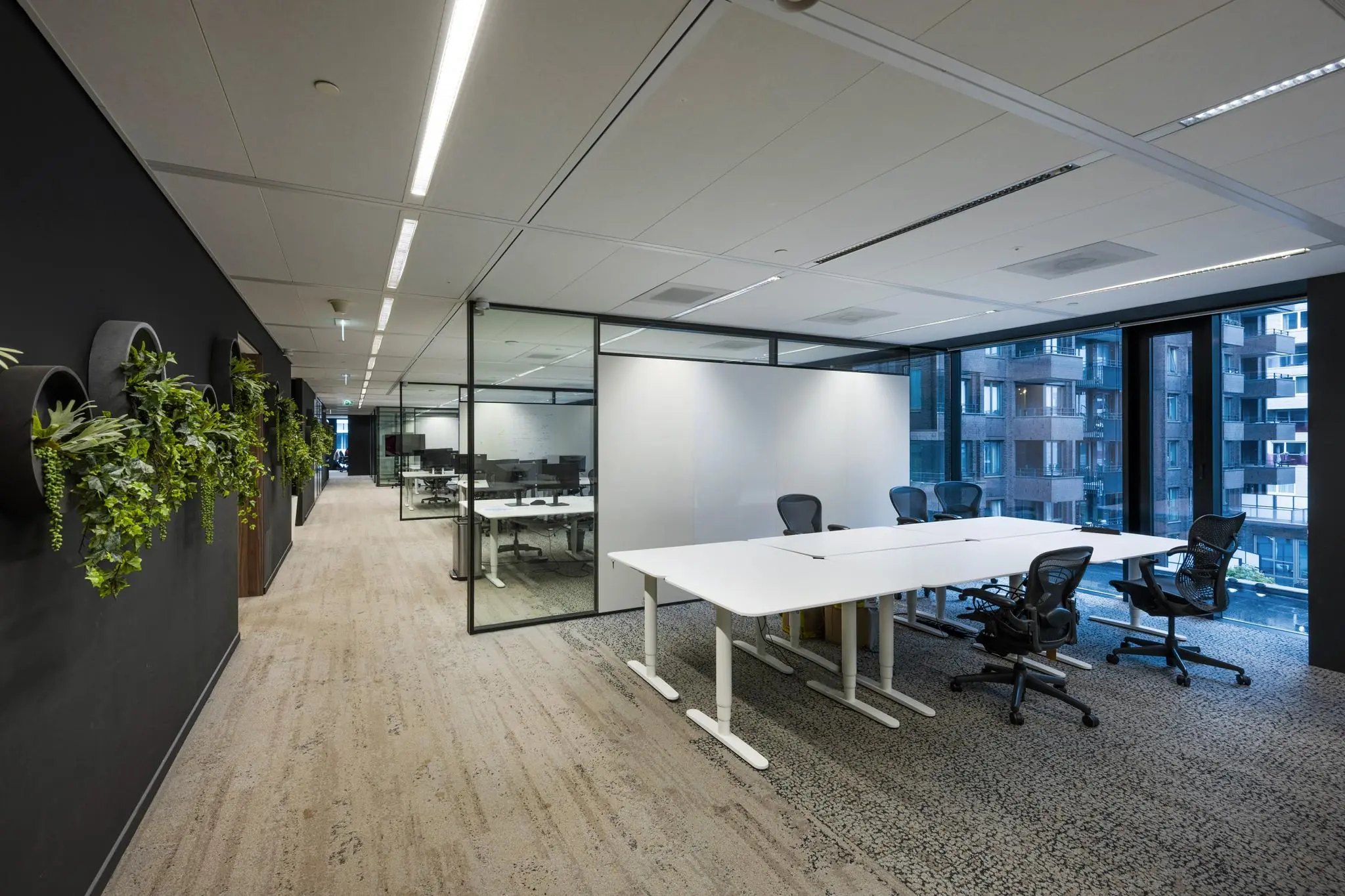 Moderne kantoorruimte aan de Gustav Mahlerlaan met glazen vergaderruimtes, ergonomische bureaustoelen en muurdecoratie met hangplanten.