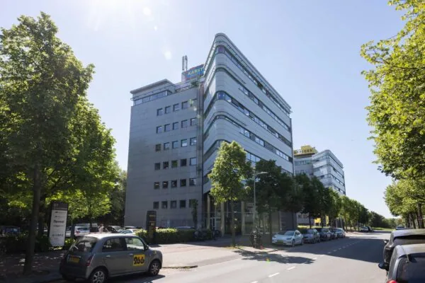 Kantoorgebouwen aan de Overschiestraat in Amsterdam op een zonnige dag, met auto's geparkeerd langs de straat.