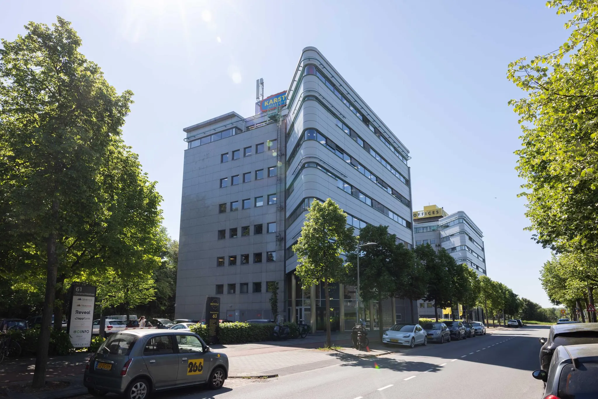 Kantoorgebouwen aan de Overschiestraat in Amsterdam op een zonnige dag, met auto's geparkeerd langs de straat.
