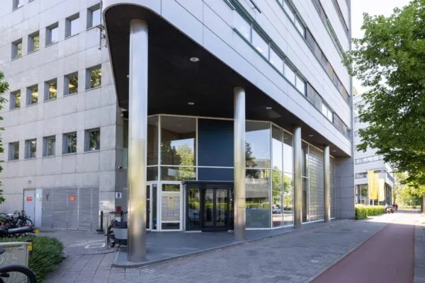 Ingang van een modern kantoorpand aan de Overschiestraat in Amsterdam met glazen gevel en stalen zuilen.