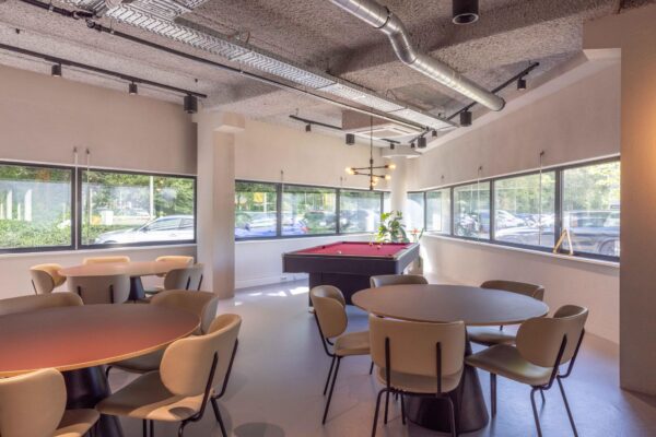 Moderne kantineruimte aan de Overschiestraat met ronde tafels, designstoelen en een pooltafel bij grote ramen.