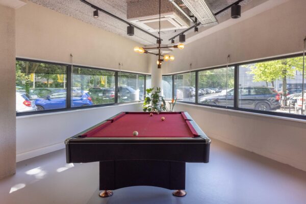 Biljarttafel met rood laken in een lichte ruimte met panoramavensters aan de Overschiestraat.