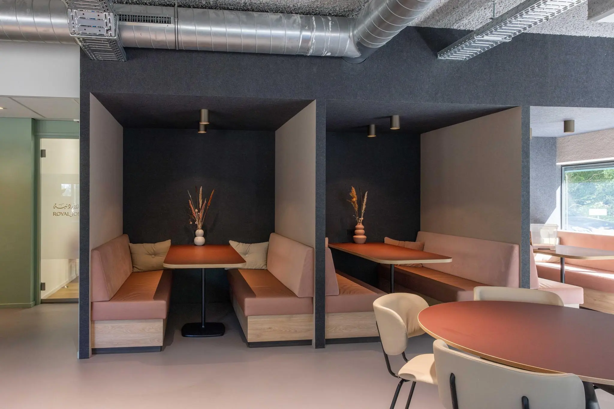 Moderne zithoeken met houten banken, terracottakleurige tafels en decoratieve vaasjes in een kantoorruimte aan de Overschiestraat.