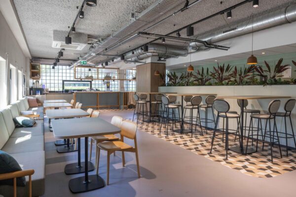 Moderne en lichte kantineruimte aan de Overschiestraat met zitgedeelte, hoge tafels en industriële plafondafwerking.