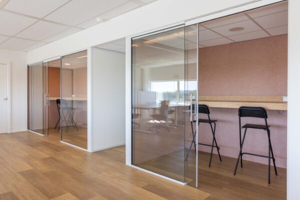 Moderne kantoorruimte aan de Overschiestraat met glazen wanden, houten vloer en werkplekken met hoge krukken.