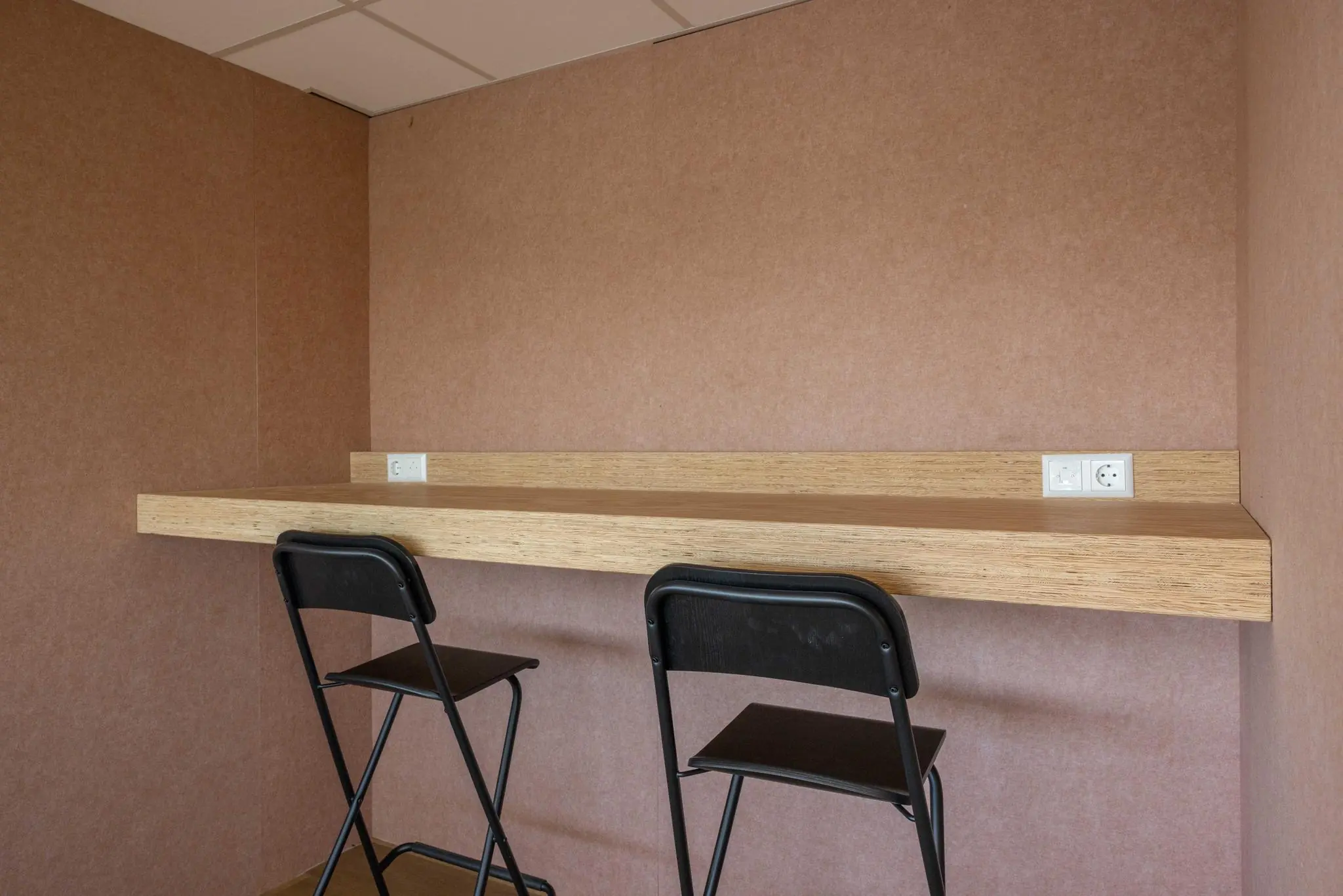 Twee zwarte barkrukken aan een houten wandtafel met stopcontacten in een minimalistisch interieur aan de Overschiestraat.