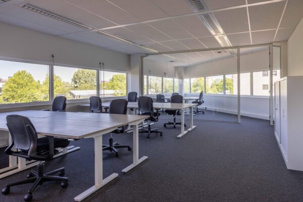 Modern kantoorinterieur aan de Overschiestraat met meerdere bureaus, bureaustoelen en grote ramen met uitzicht op groen.