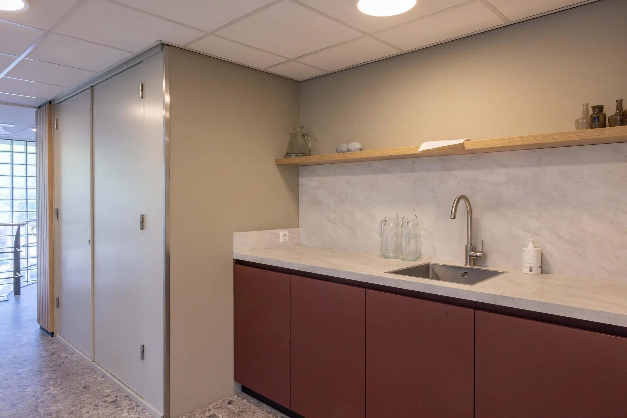 Moderne pantry met marmeren achterwand, donkerrode kasten en een rvs-kraan in een gebouw aan de Overschiestraat.