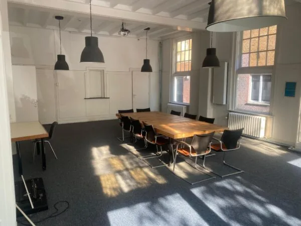 Vergaderruimte op de Gasthuisplaats met grote houten tafel, zwarte stoelen en veel natuurlijk licht.