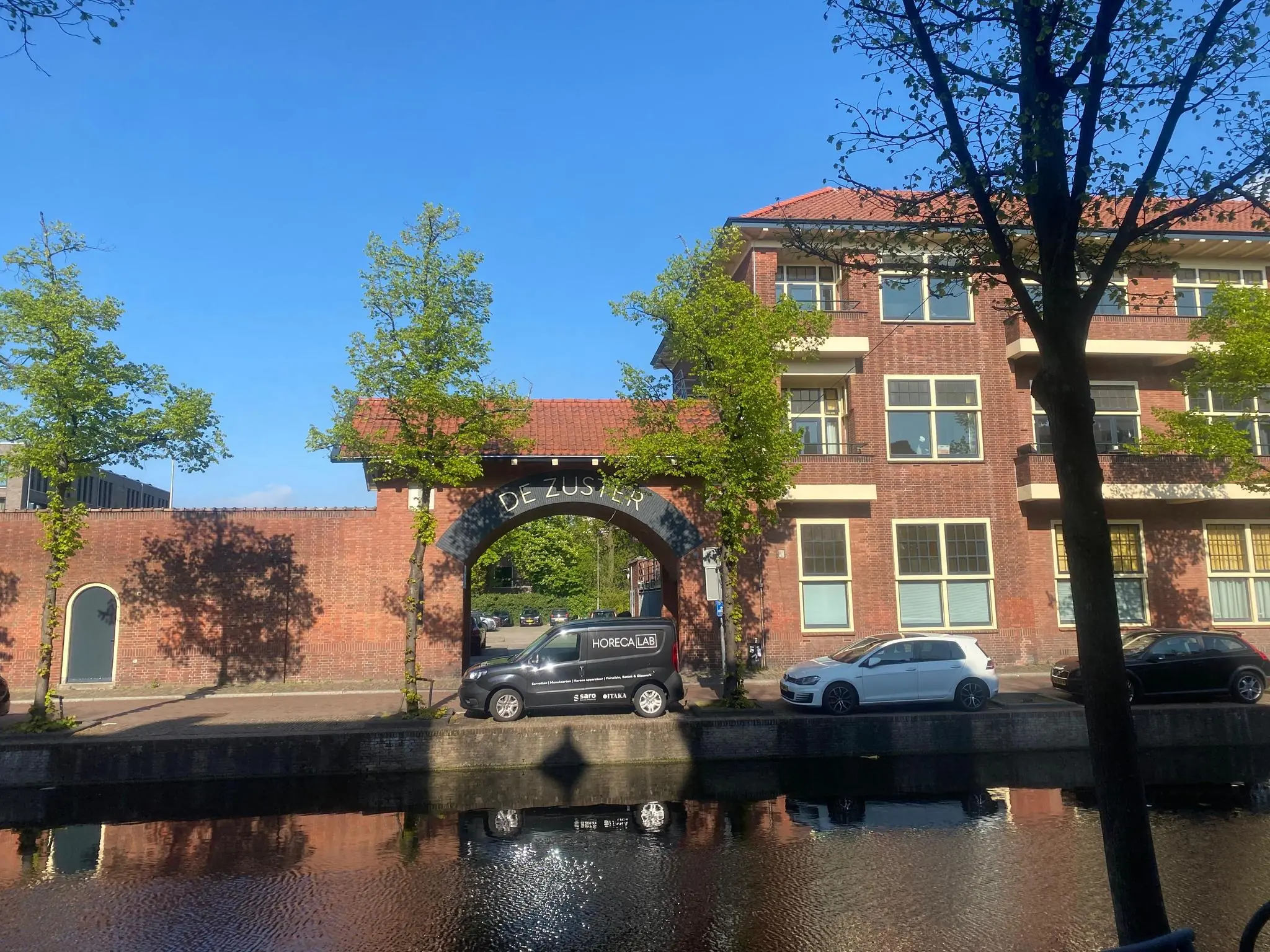Gebouw met een poort met de tekst "De Zuster" aan de Gasthuisplaats, gezien vanaf de overkant van een gracht.