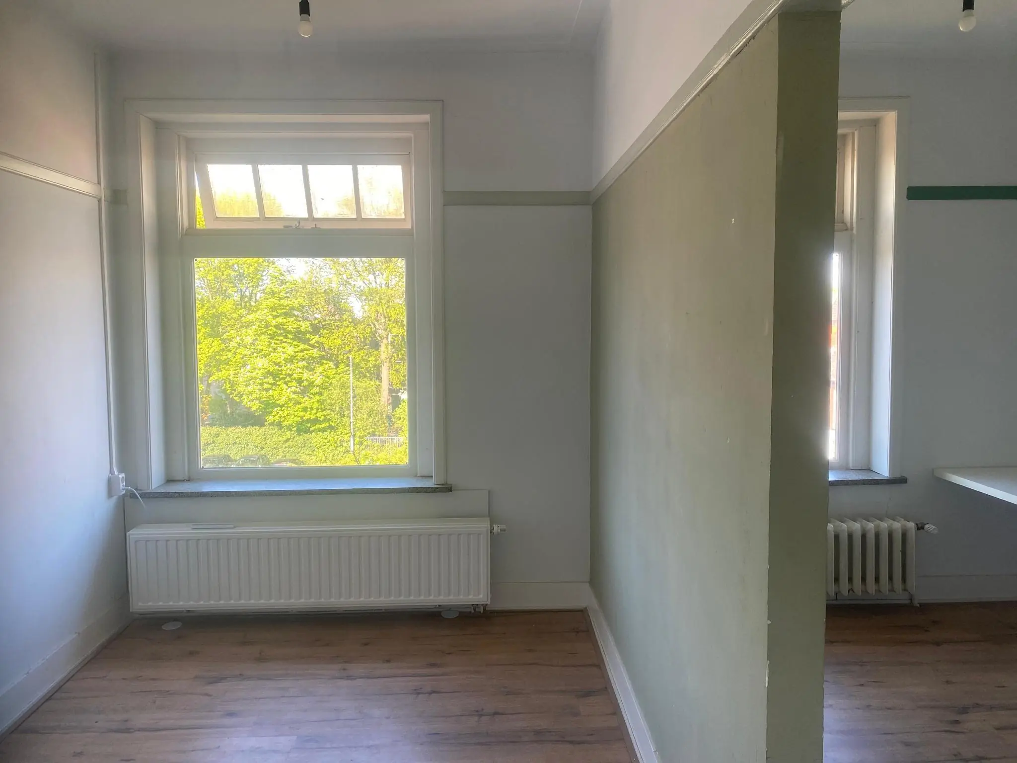 Lichte kamer aan de Gasthuisplaats met houten vloer, grote ramen en een scheidingsmuur.
