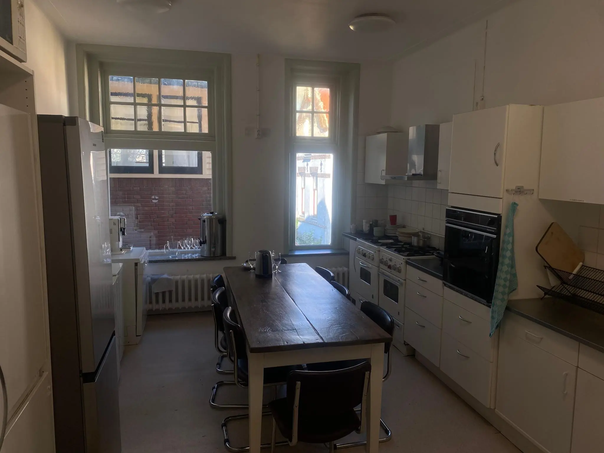 Gemeenschappelijke keuken aan de Gasthuisplaats met lange eettafel, gaskooktoestellen, oven en koffiezetapparaten bij het raam.
