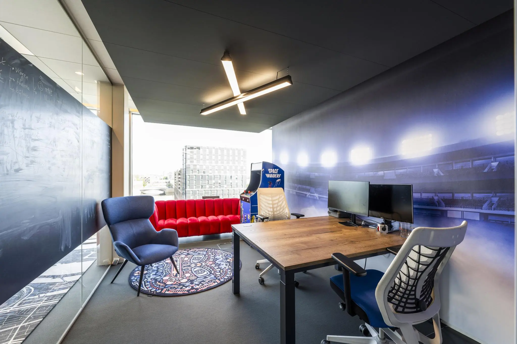 Modern kantoorinterieur aan de Krijn Taconiskade met werkplek, rode bank, arcadekast en stadionmuurdecoratie.
