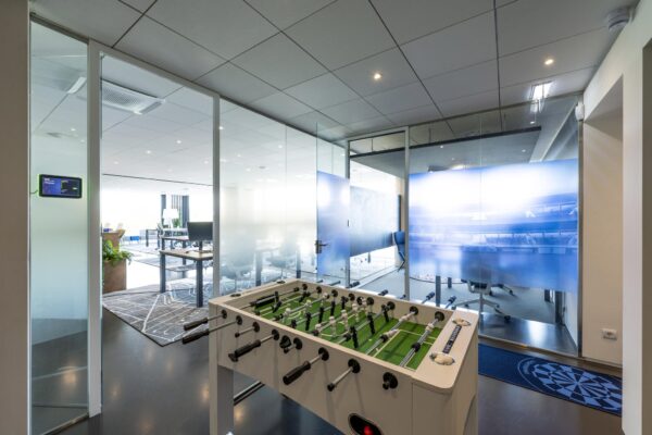 Moderne kantoorruimte aan de Krijn Taconiskade met glazen vergaderruimtes en een tafelvoetbaltafel op de voorgrond.