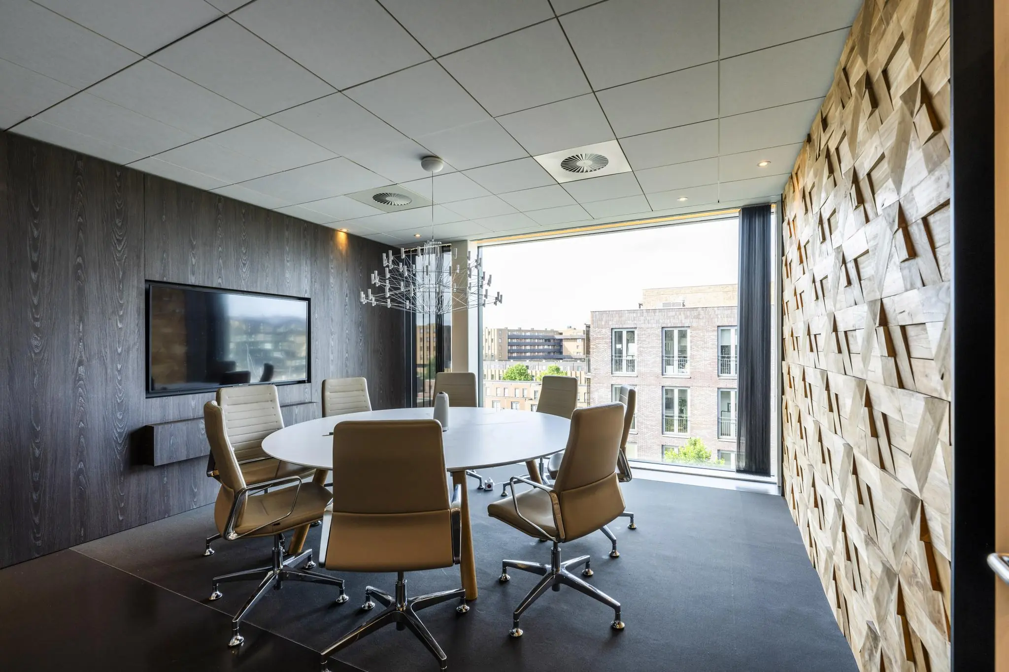 Modern ingerichte vergaderkamer aan de Krijn Taconiskade met grote ronde tafel, designstoelen, houten accentmuur en uitzicht op omliggende gebouwen.