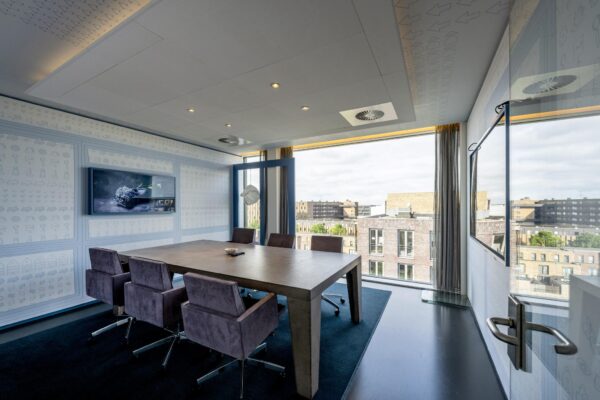 Vergaderruimte met zes stoelen, een houten tafel, een flatscreen en uitzicht op de Krijn Taconiskade in Amsterdam.