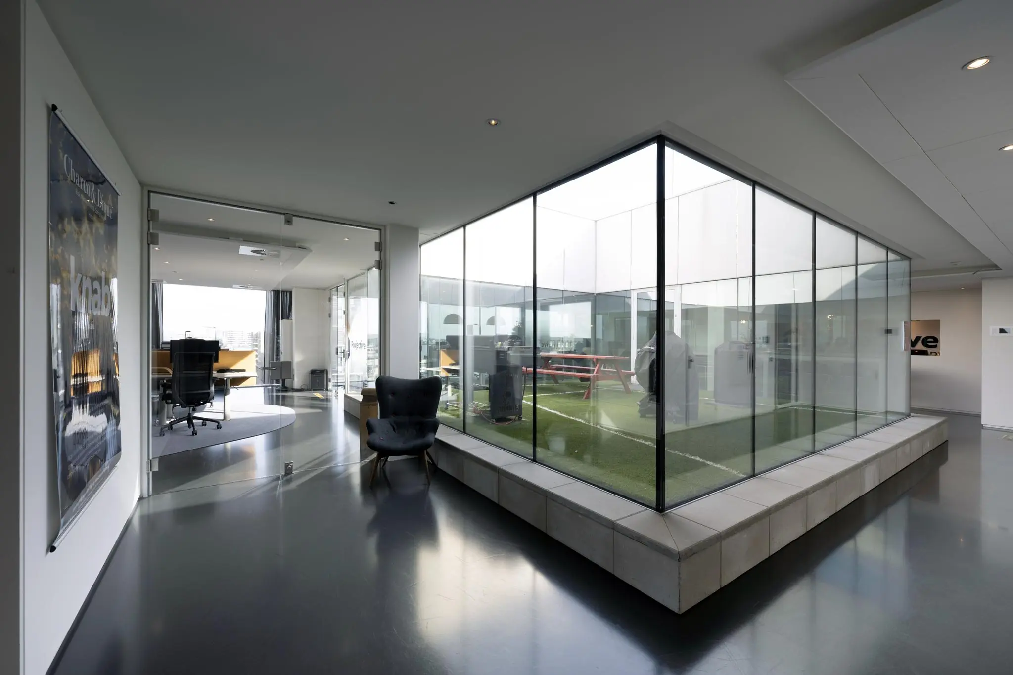Modern kantoorinterieur aan de Krijn Taconiskade met glazen vergaderruimtes en een binnentuin met kunstgras.