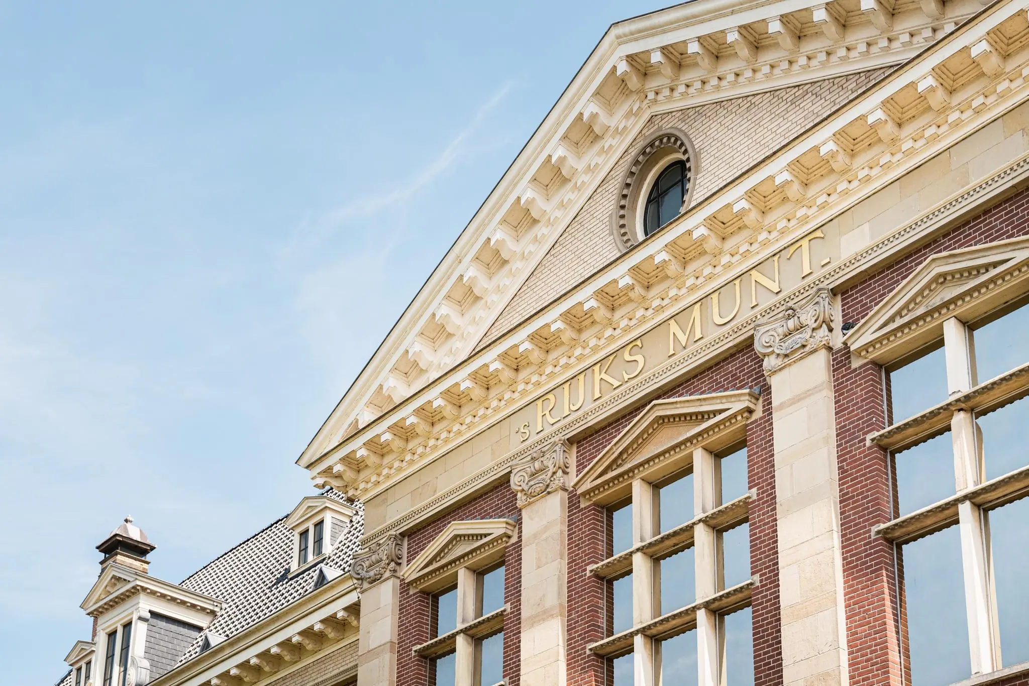 Voorgevel van het historische gebouw 's Rijks Munt aan de Leidseweg, met klassieke architectuur en goudkleurige belettering.