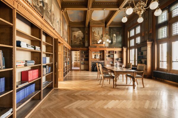 Historische bibliotheekruimte aan de Leidseweg met houten boekenkasten, muurschilderingen en een lange leestafel.