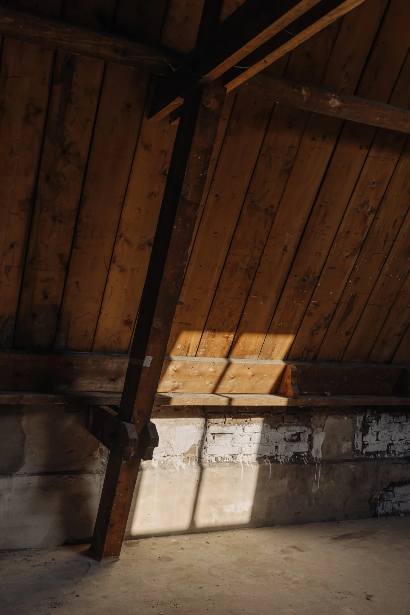 Zolderruimte met een houten schuin dak en een gemetselde muur aan de Leidseweg, verlicht door zonlicht.