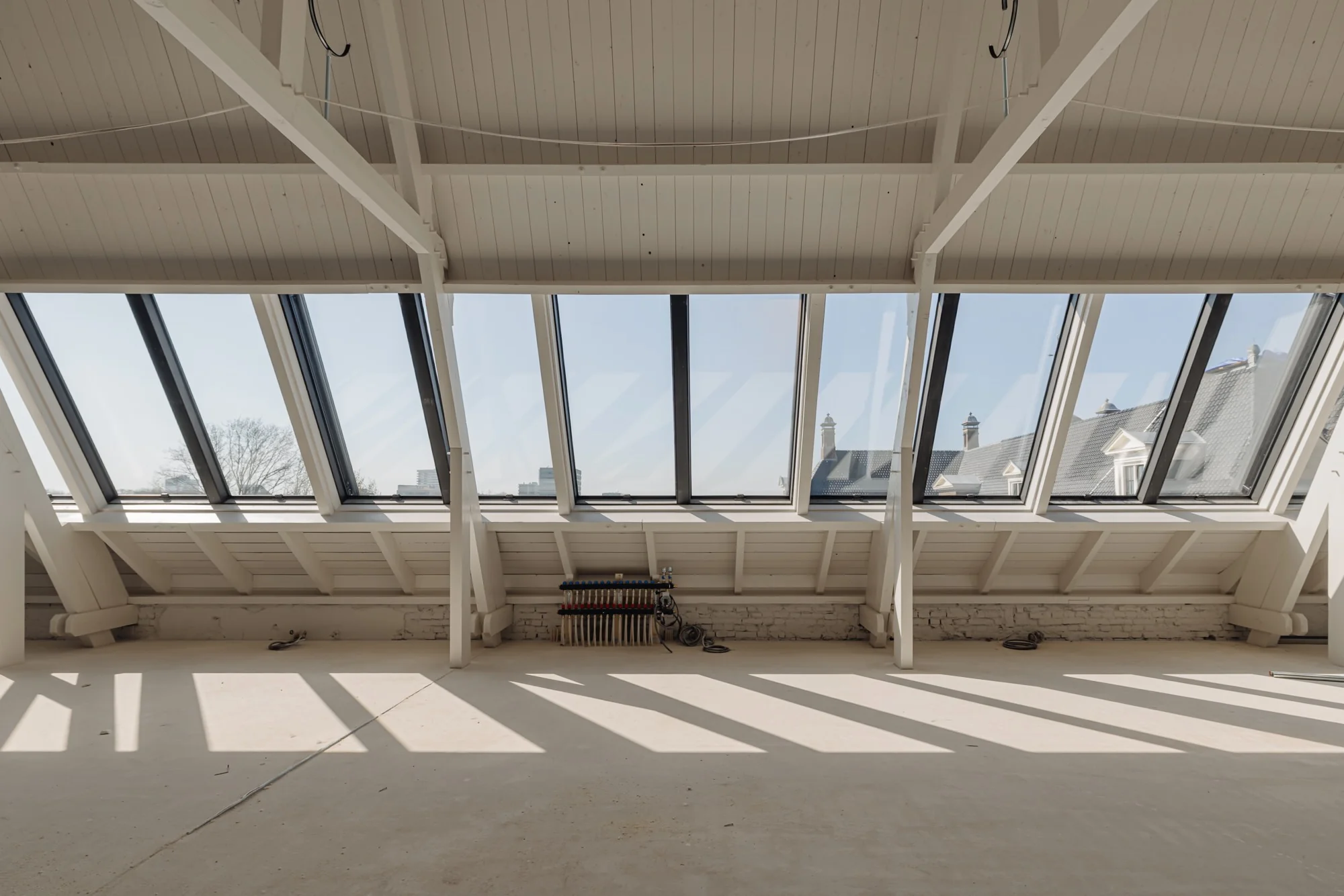 Lichte zolderruimte aan de Leidseweg met grote schuine dakramen en zicht op omliggende daken.