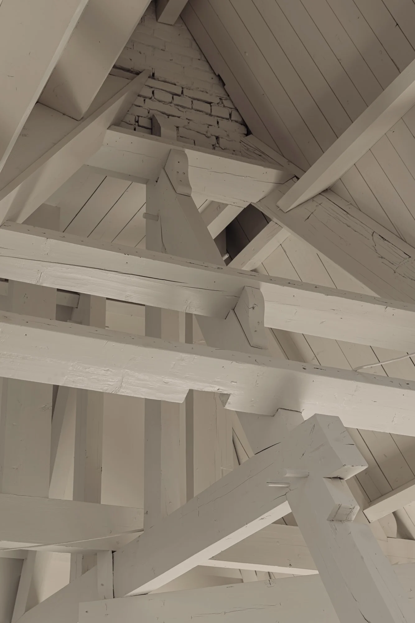 Houten kapconstructie met zichtbare houten balken en witgeschilderde spanten in het dak van een gebouw aan de Leidseweg.