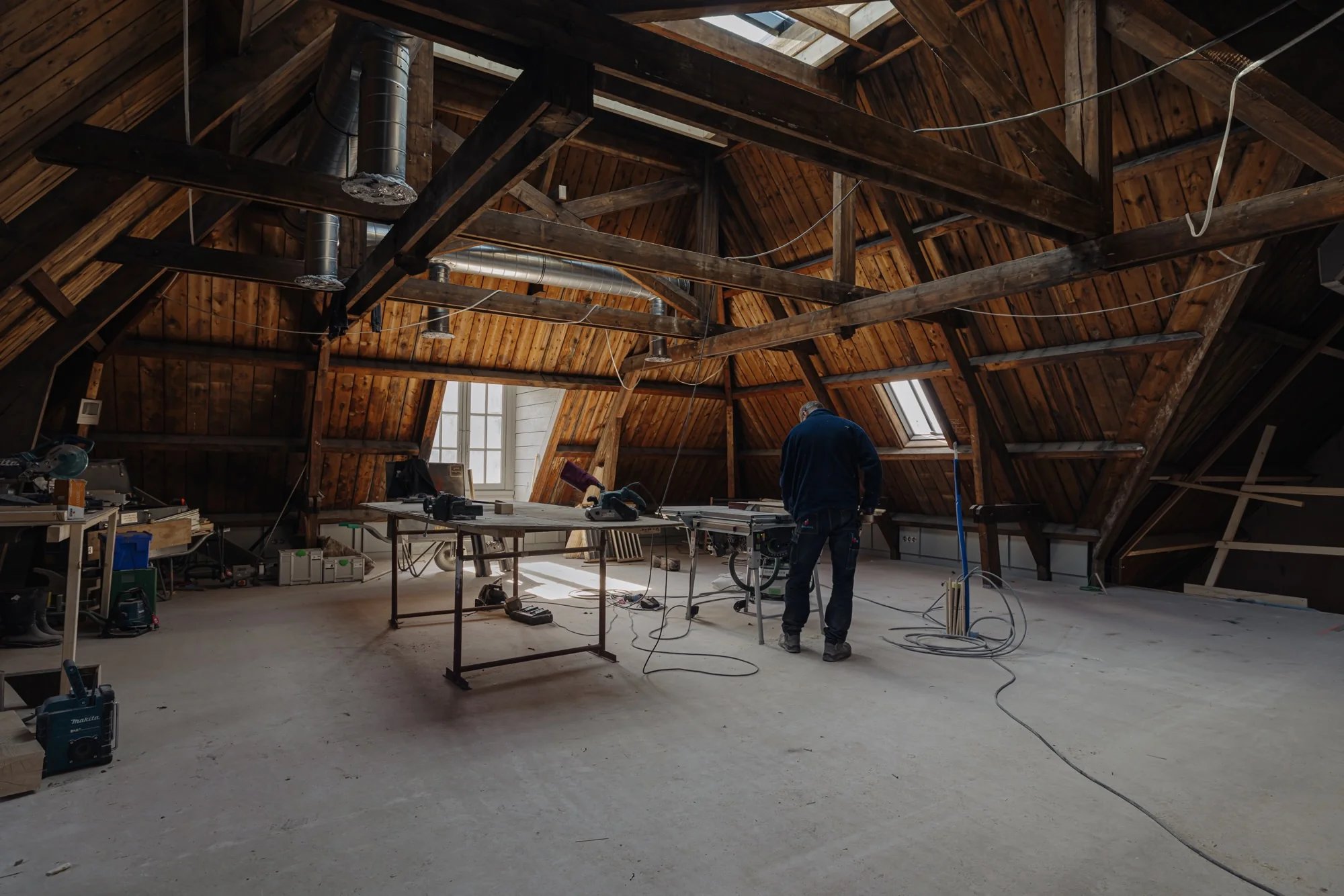 Man aan het werk in een ruime, houten zolderruimte met werkbanken en gereedschap aan de Leidseweg.