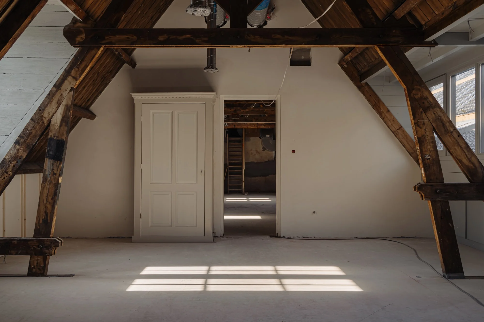 Zicht op een zolderruimte aan de Leidseweg met houten balken, een witte inbouwkast en een deuropening naar een achterliggende kamer.