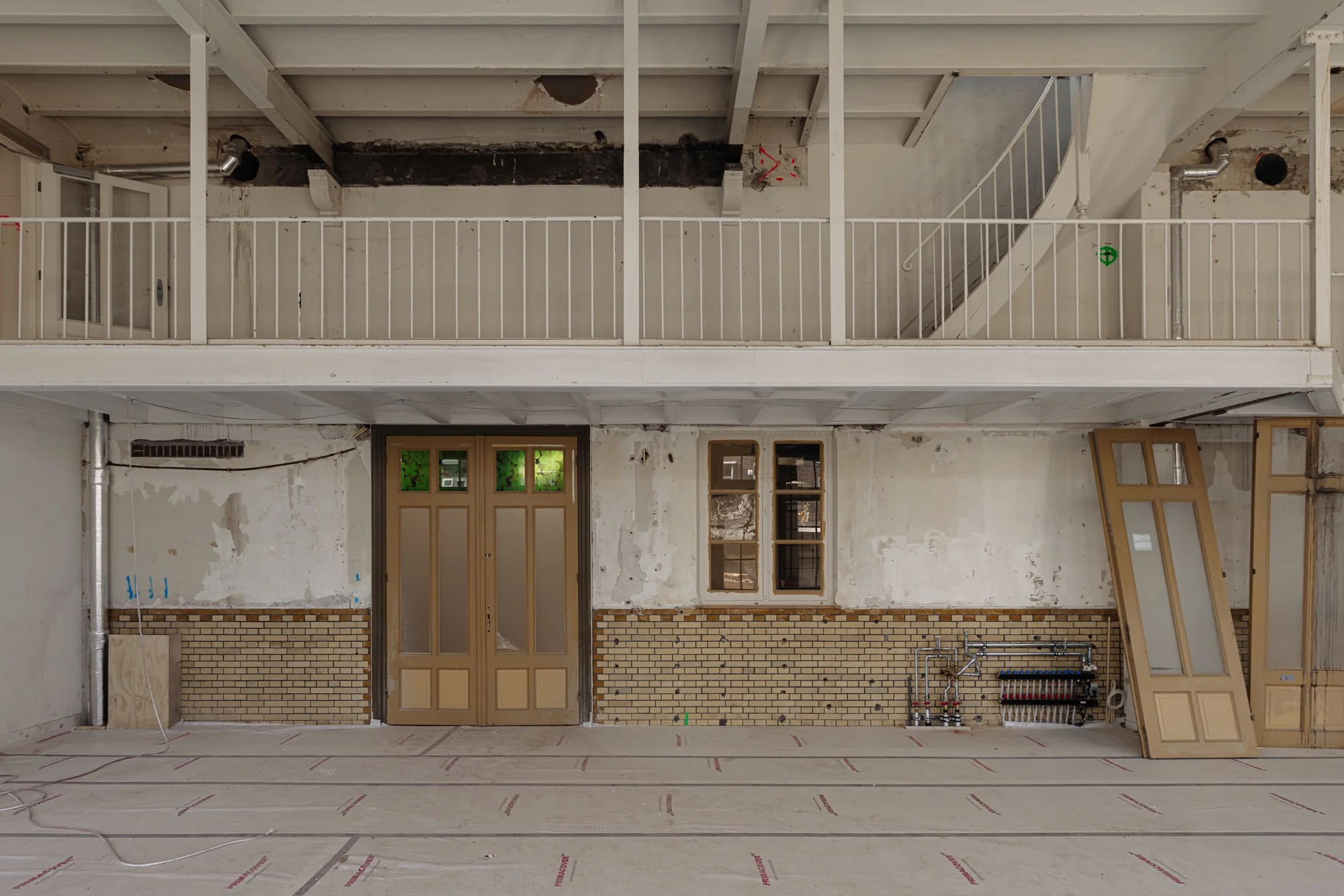 Binnenzicht van een renovatiepand aan de Leidseweg met een halfopen verdiepingsvloer, houten deuren, en onafgewerkte muren met gele baksteen.