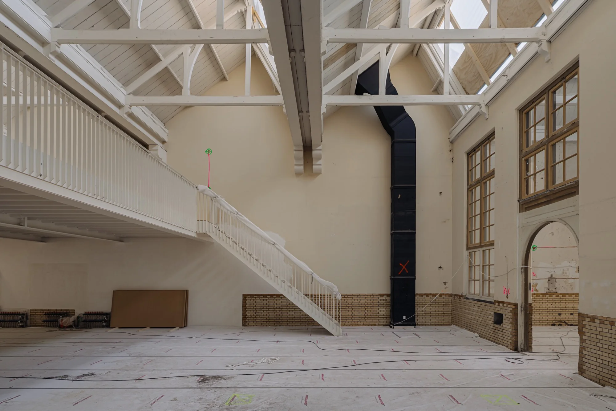 Interieur van een oud schoolgebouw aan de Leidseweg in renovatie, met hoge plafonds, houten balken en een trap naar een entresol.