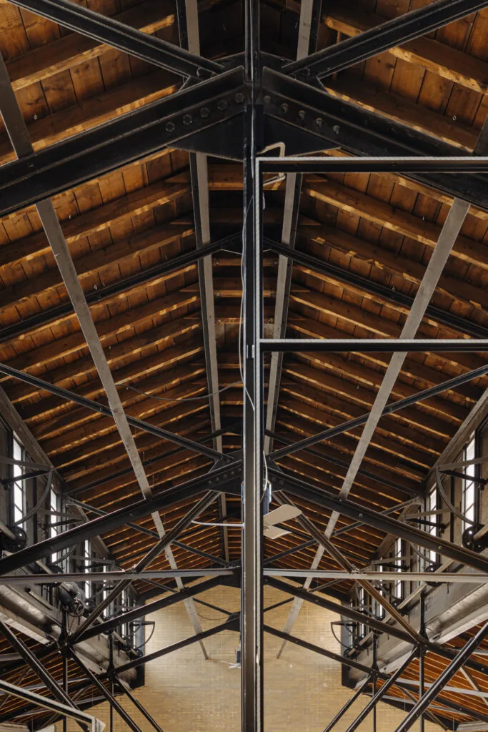 Interieur van een industriële loods aan de Muntkade met houten dakconstructie en stalen spanten.