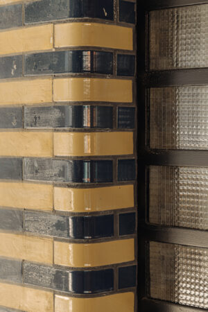 Detail van een gebogen hoek van een gevel aan de Muntkade met glanzende geel-blauwe bakstenen en glasbouwstenen.